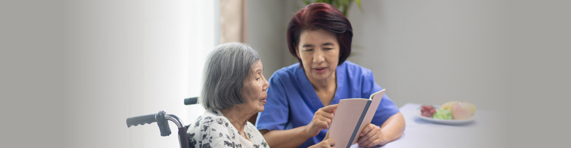 Elderly woman reading aloud a book for dementia therapy with caregiver.